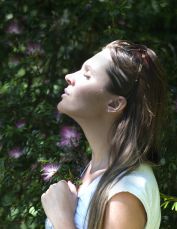 Woman Closing Her Eyes Against Sun Light Standing Near Purple Petaled Flower Plant