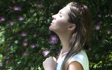 Woman Closing Her Eyes Against Sun Light Standing Near Purple Petaled Flower Plant